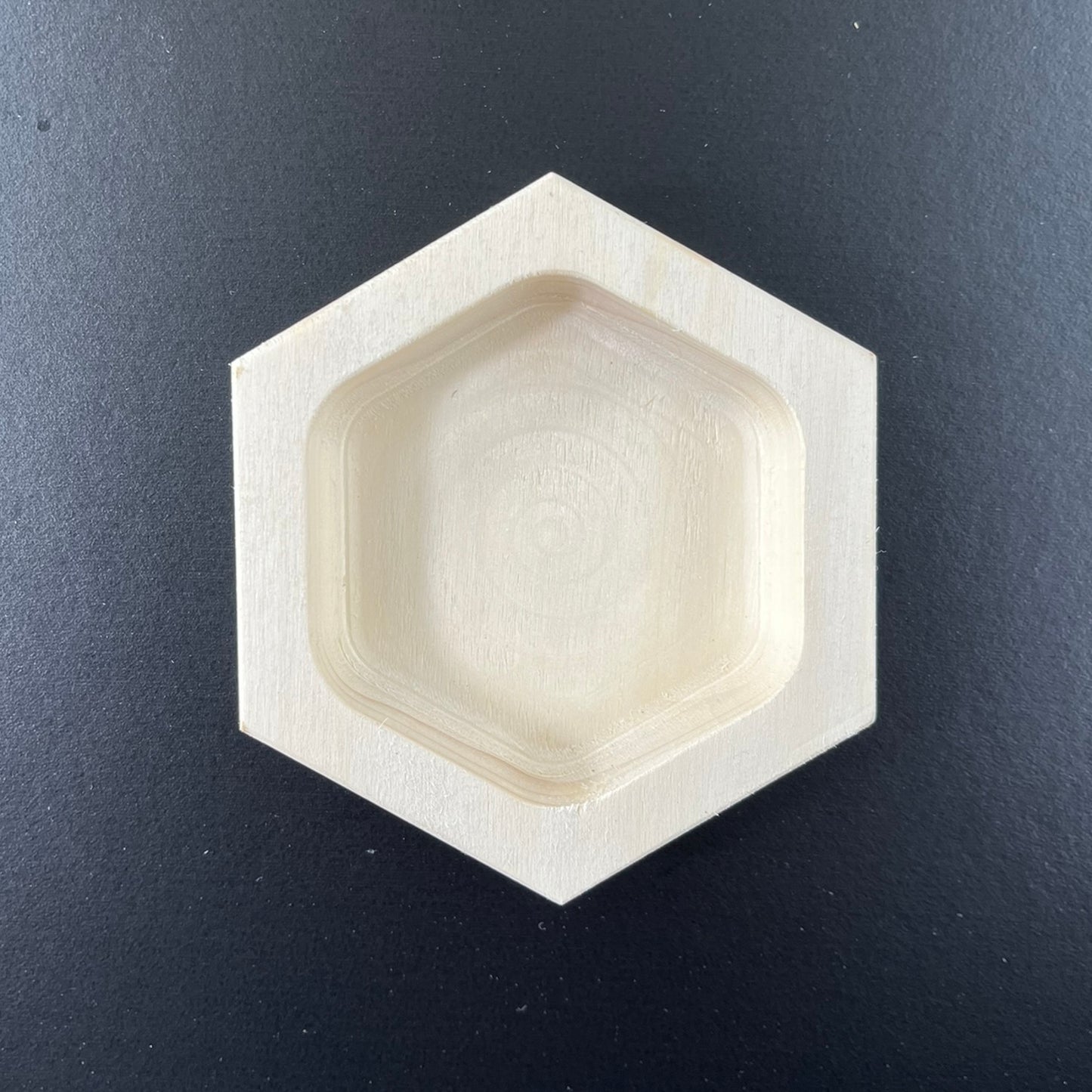 White hexagonal wooden tray with rounded interior cavity, viewed from above against dark gray background.