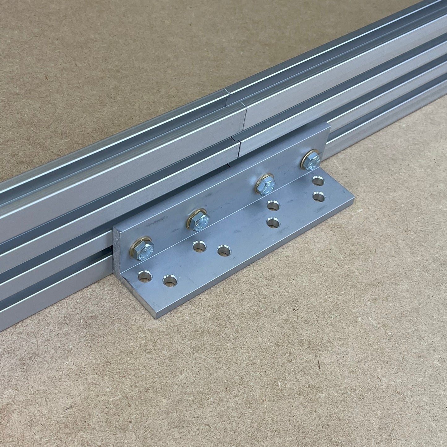 A metal track connector kit from Woodhaven, consisting of a flat metal bracket and bolts, placed on a flat surface with two tracks aligned parallel to each other.